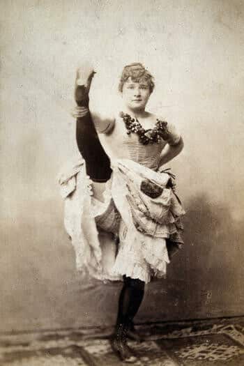 Photographie en noir et blanc de La Goulue qui lève la jambe dans un studio de photographie.