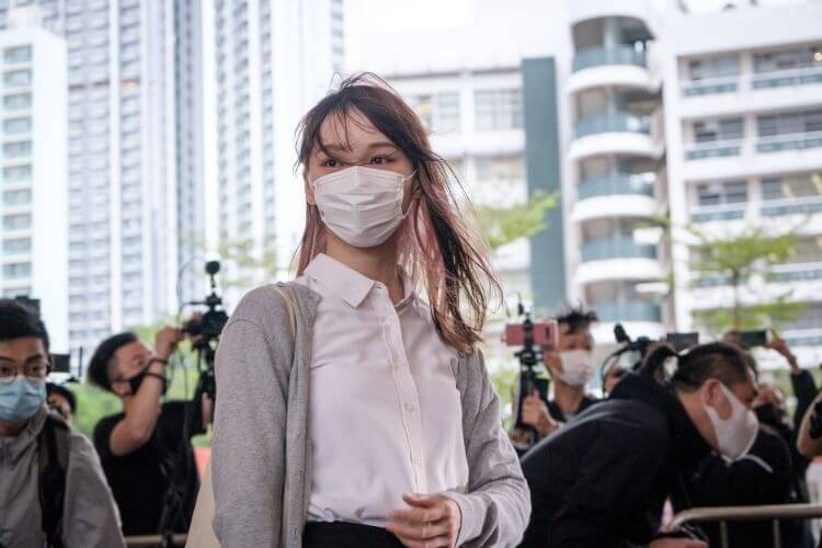 Photographie d’Agnes Chow et de journalistes. Elle porte un masque chirurgical.